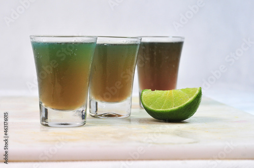 three drink dose of absinthe, tequila and vodka with lemon in the glass cup on the table, horizontal image with blurred background
