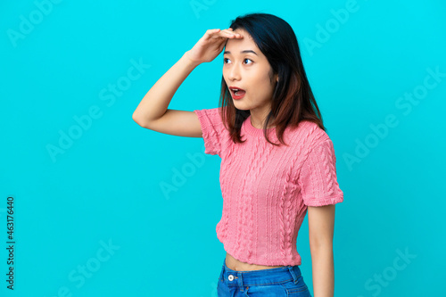 Young Vietnamese woman isolated on blue background with surprise expression while looking side