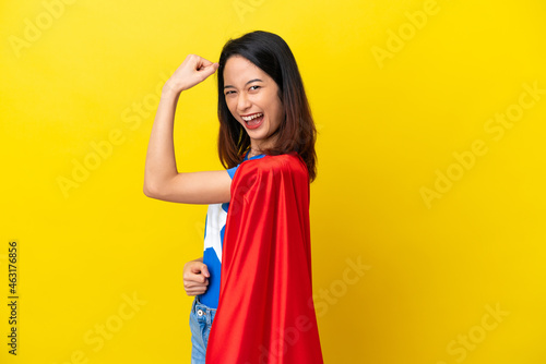 Super hero Vietnamese woman isolated on yellow background doing strong gesture