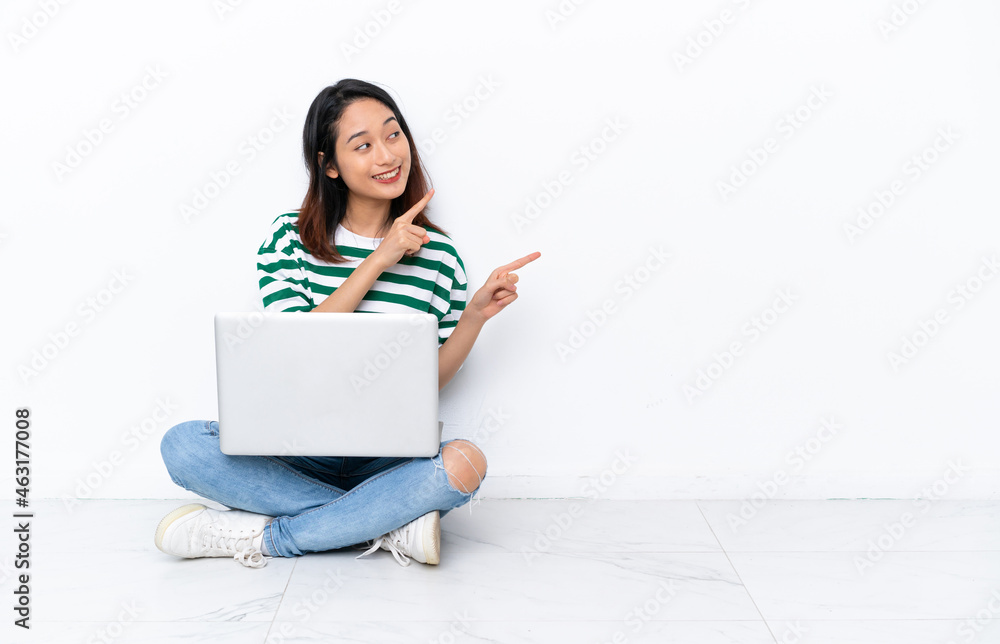 Young Vietnamese woman with a laptop sitting on the floor isolated on white wall pointing with the index finger a great idea Young Vietnamese woman with a laptop sitting on the floor isolated on white wall pointing with the index finger a great idea