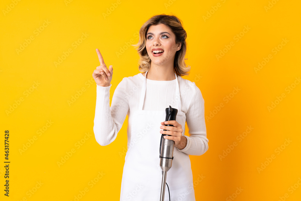 Girl using hand blender isolated on yellow background pointing away Girl using hand blender isolated on yellow background pointing away