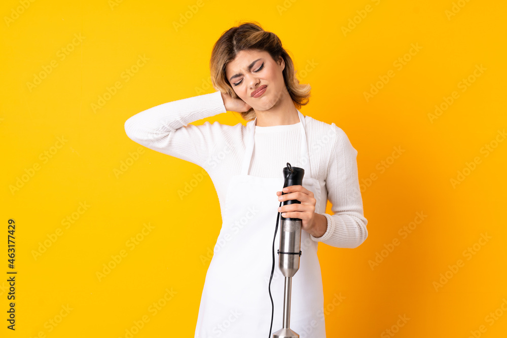 Girl using hand blender isolated on yellow background with neckache