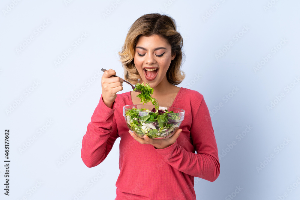 Teenager woman with salad isolated on blue background Teenager woman with salad isolated on blue background