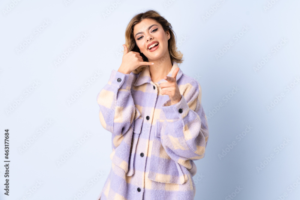 Young Russian woman isolated on blue background making phone gesture and pointing front Young Russian woman isolated on blue background making phone gesture and pointing front