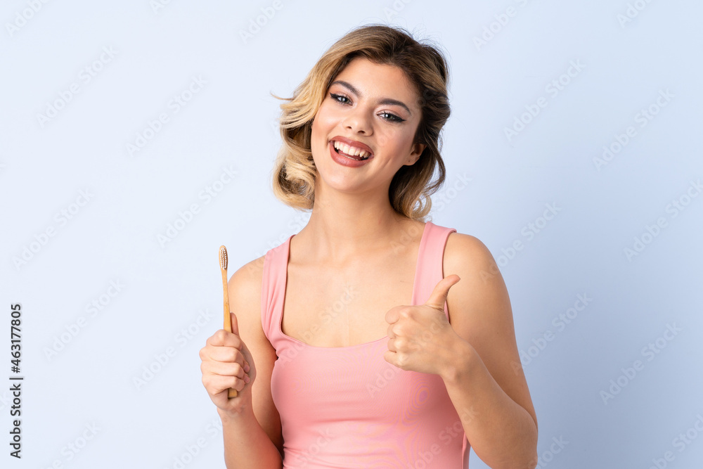 Teenager girl brushing her teeth isolated on blue background with thumbs up because something good has happened Teenager girl brushing her teeth isolated on blue background with thumbs up because something good has happened