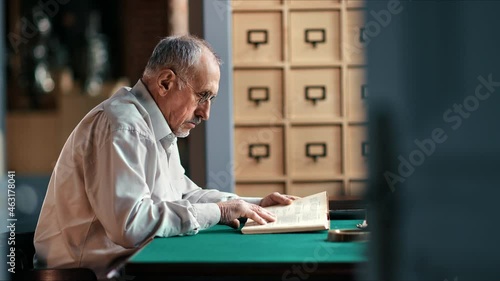 Elderly 70s male lawyer reading juristic book searching legal information working at public library photo