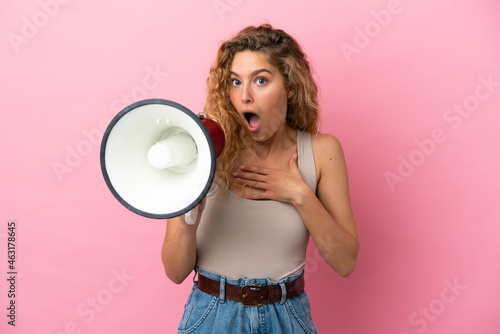 Young blonde woman isolated on pink background shouting through a megaphone with surprised expression