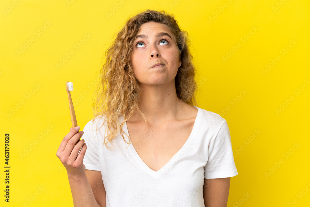 Young caucasian woman holding a brushing teeth isolated on yellow background and looking up Young caucasian woman holding a brushing teeth isolated on yellow background and looking up