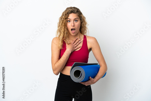 Young sport blonde woman going to yoga classes while holding a mat isolated on white background surprised and shocked while looking right