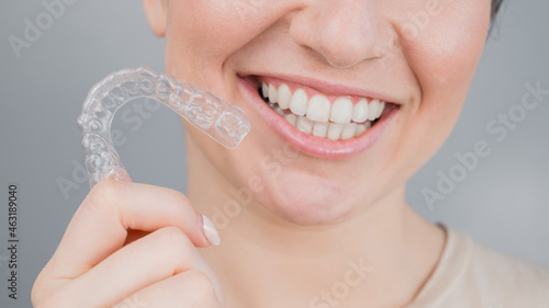 Close-up portrait of a woman putting on a transparent plastic retainer. A girl corrects a bite with the help of an orthodontic device photo