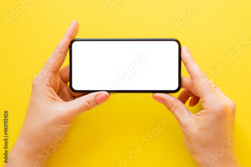 Mobile phone with empty white screen held in hands horizontally on yellow background