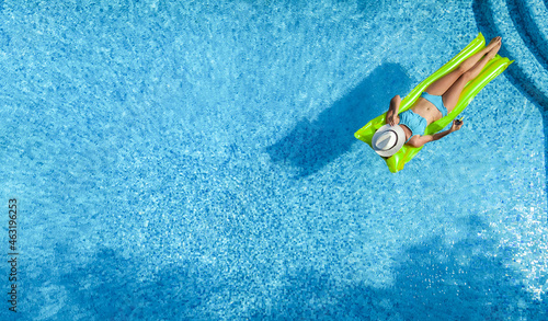 Beautiful young woman relaxing in swimming pool, girl swims on inflatable mattress and has fun in water on family vacation, tropical holiday resort, aerial drone view from above 
