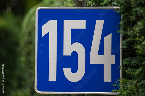 A blue house number plaque, showing the number one hundred fifty four, 154 on the street in Austria