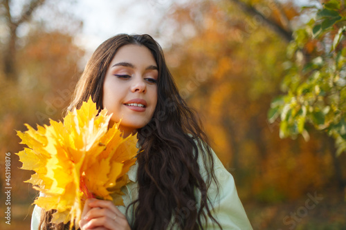 A happy young woman in an autumn park with a bunch of maple leaves in hands