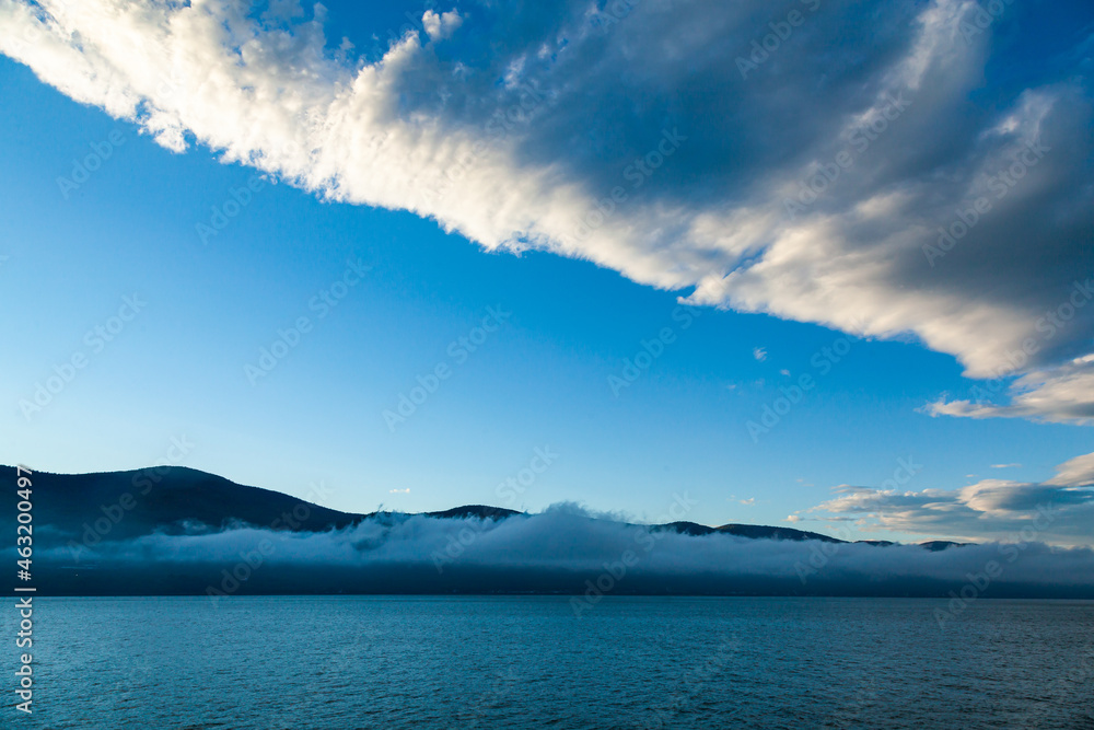 Early morning in the sea bay against the background of mountains, blue sky and fog in the distance rising above the water. Early morning in the sea bay against the background of mountains, blue sky and fog in the distance rising above the water.