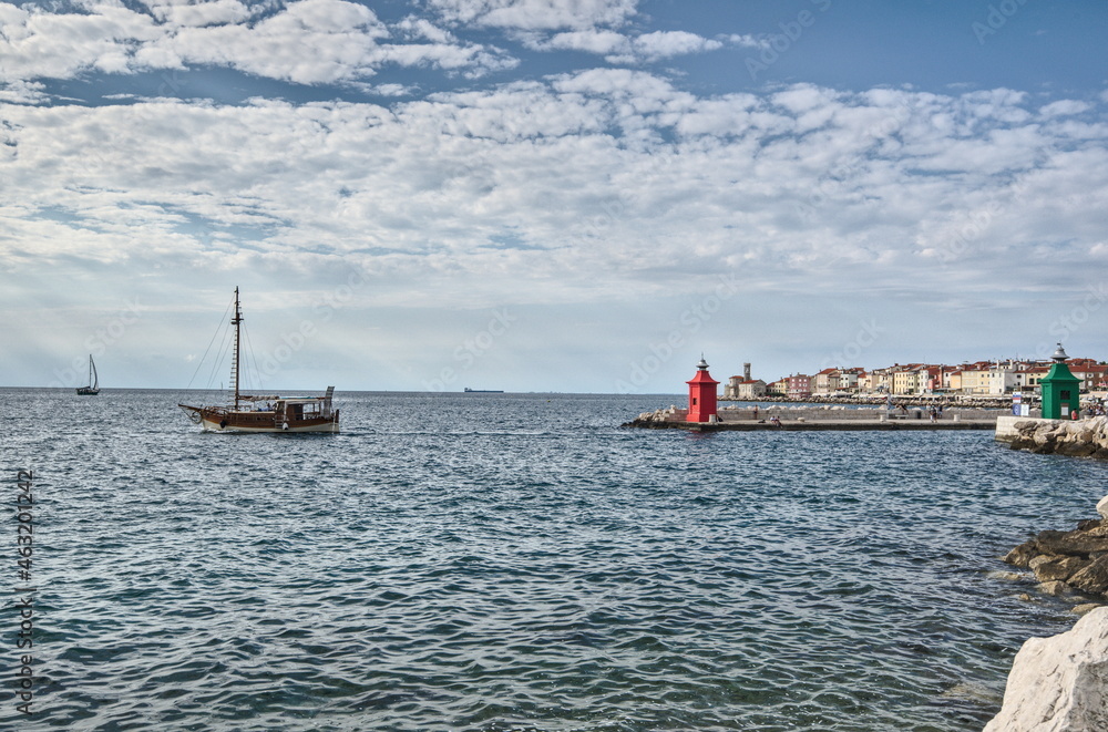 View of the red and green lighthouses on a pier,  boat and the architecture of  the city on the horizon, Piran, Slovenia.