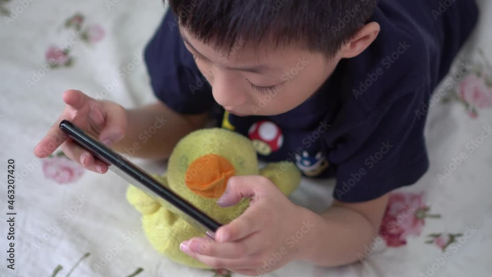 Asia kid play mobile phone accompanied by old yellow duck plush toy Asia kid play mobile phone accompanied by old yellow duck plush toy