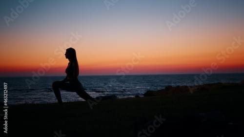 Silhouette of fitness young woman stretching legs after active workout on beach. Beautiful summer sunset over ocean. Concept of healthy and active lifestyles. © GRAFStock