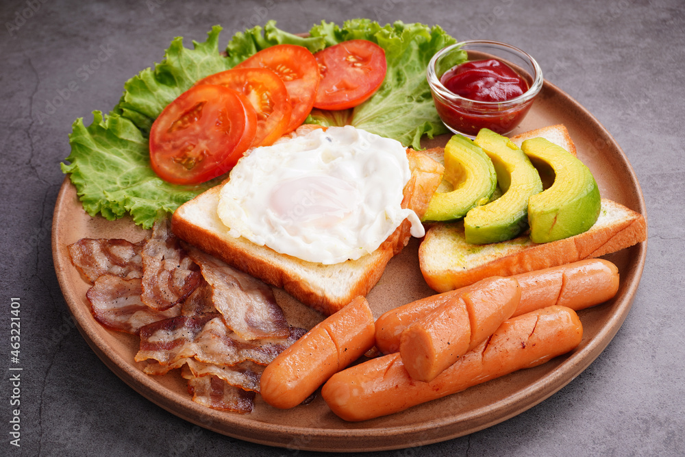 European breakfast toast eggs bacon  ​​sliced ​​tomatoeswith hot dog and vegetables in a round plate.