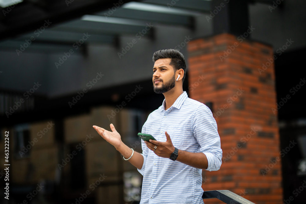Φωτογραφία Confident businessman with smartphone in his hands wearing earphones and listening music or podcast outdoors, sitting on stairs near office