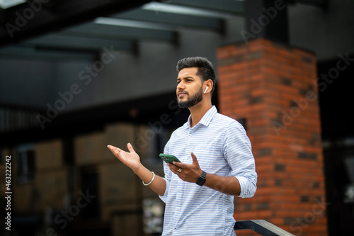 Confident businessman with smartphone in his hands wearing earphones and listening music or podcast outdoors, sitting on stairs near office.