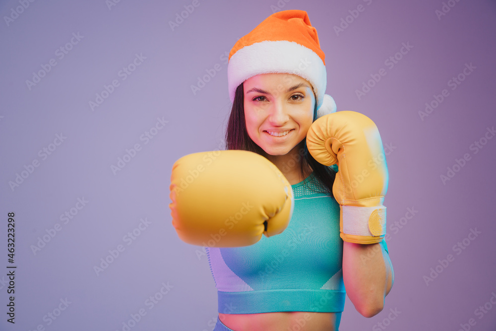 Close up photo of strong sportswoman in boxing gloves and Christmas hat, boxer posing. isolated on gradient studio background in neon light. Beautiful caucasian woman practicing Close up photo of strong sportswoman in boxing gloves and Christmas hat, boxer posing. isolated on gradient studio background in neon light. Beautiful caucasian woman practicing
