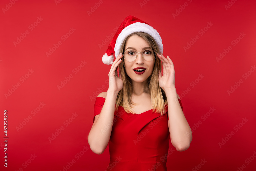 Photo of attractive woman in Christmas hat and red dress, holds glasses with surprised. Isolated over red background Photo of attractive woman in Christmas hat and red dress, holds glasses with surprised. Isolated over red background