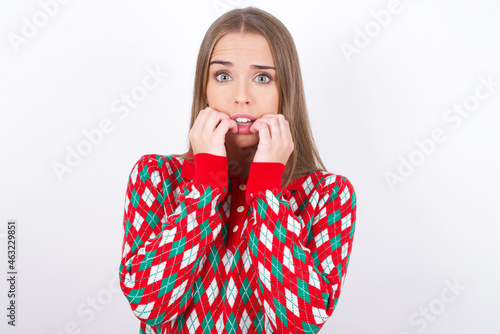 Anxiety - Young caucasian girl wearing christmas sweaters on white background covering his mouth with hands scared from something or someone bitting nails. photo