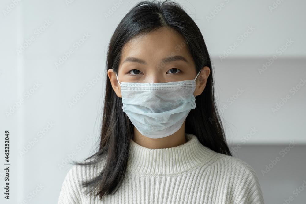 Young Asian woman in a protective medical mask to protect against viral diseases looks into the camera. The concept of health, safety and pandemic Young Asian woman in a protective medical mask to protect against viral diseases looks into the camera. The concept of health, safety and pandemic