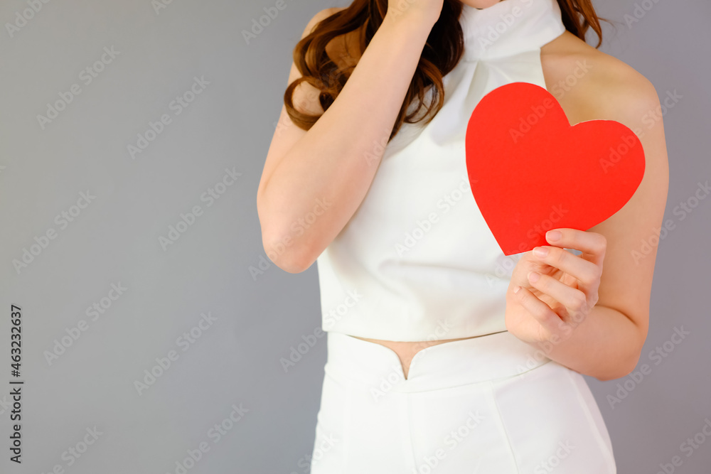Portrait beautiful asian woman on gray background, valentine day in love concept, model holding red heart sign in hand