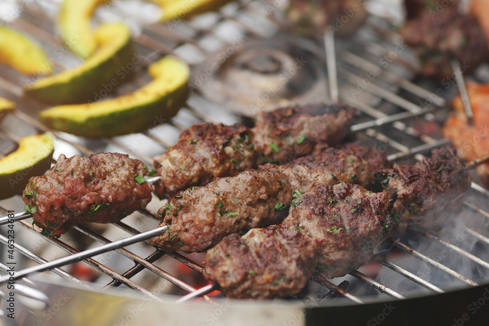 narrow closeup on fresh kofta lamb meat spits and pumpkin slices that are grilled on a charcoal grill - barbecue scenery with selective focus