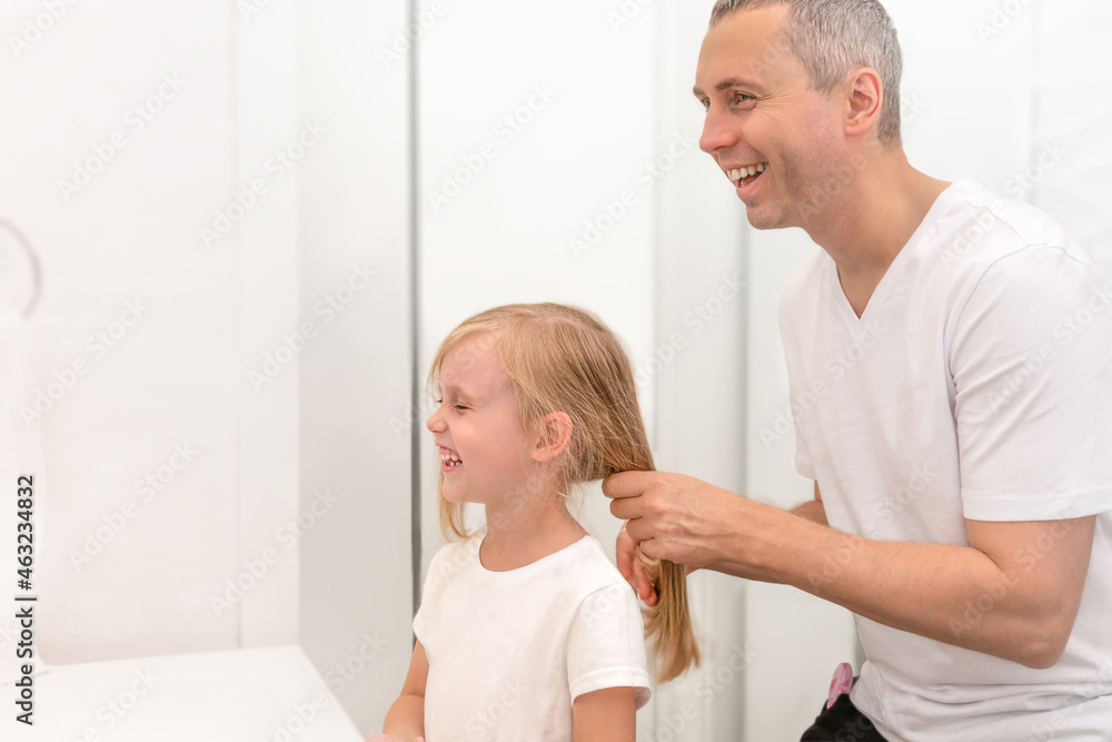 Dad is combing his daughter's hair. The girl and the man laugh and look in the mirror.