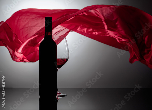 Вottle and glass of red wine on a black reflective background.
