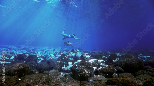 Girl swimming with turtle in rays of light underwater