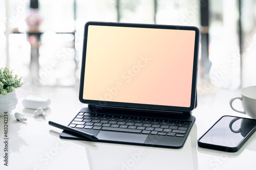 blank screen tablet with magic keyboard and smartphone on white table in office room.