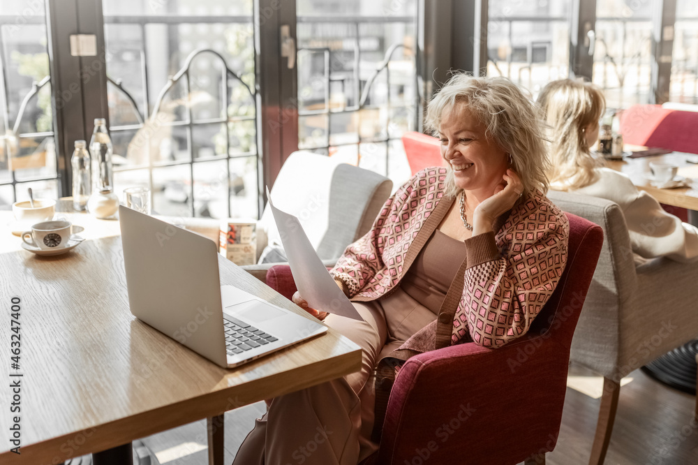An attractive adult blonde of European appearance looks through documents sitting at a table in a cafe An attractive adult blonde of European appearance looks through documents sitting at a table in a cafe