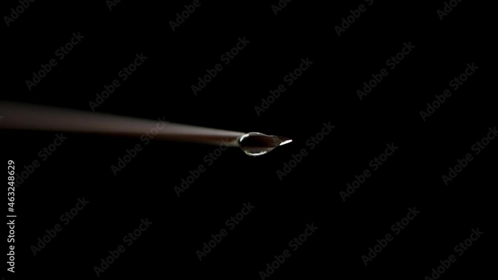 Drop Of Liquid On Needle Tip on Black Background. Drop Falling in Slow Motion, Macro Shooting Drop Of Liquid On Needle Tip on Black Background. Drop Falling in Slow Motion, Macro Shooting