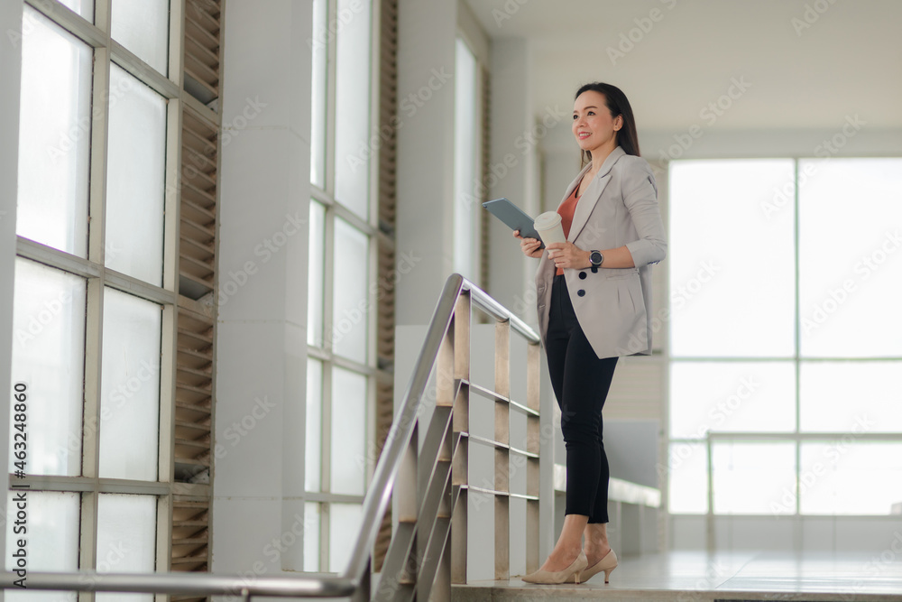 Portrait of an Asian businesswoman in a suit holding coffee and digital tablet in the office. Portrait of an Asian businesswoman in a suit holding coffee and digital tablet in the office.