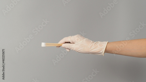 Cotton sticks for swab test in hand with white medical gloves on grey background.