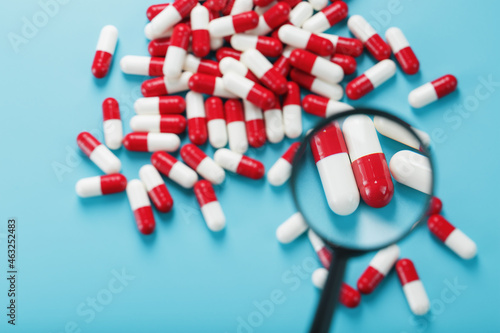A handful of Red and white pill capsules are examined with a magnifying glass on a blue background photo