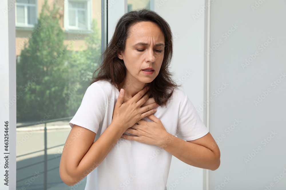 Mature woman suffering from breathing problem near window indoors Mature woman suffering from breathing problem near window indoors