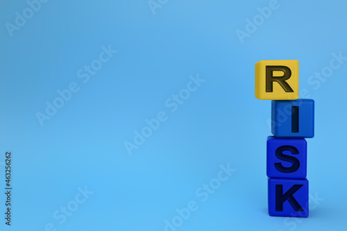 Stack of color wooden cubes with word Risk on light blue background. Space for text