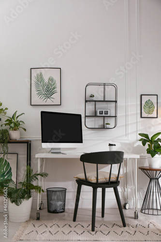 Comfortable workplace with modern computer and houseplants in room. Interior design