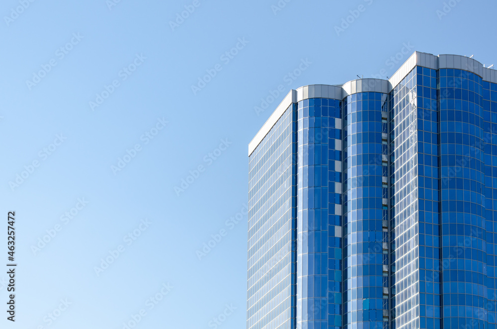 Fototapeta premium altitudinal building with a blue glass facade against a clear, light blue sky. multistory residential building, stylish building, modern style of architecture. space for text