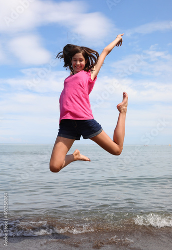 young girl with brown hair jumping very happy by the sea in summer
