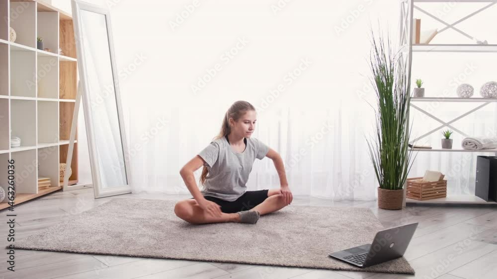 Flexibility training. Online lesson. Teenager sport. Pretty girl doing stretching workout butterfly looking laptop in light room interior. Flexibility training. Online lesson. Teenager sport. Pretty girl doing stretching workout butterfly looking laptop in light room interior.