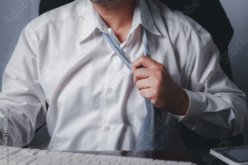 Close up portrait of exhausted frustrated stressed handsome sad unhappy upset entrepreneur trying to take off uncomfortable tie formal wear isolated at office., tired businessman taking off necktie.