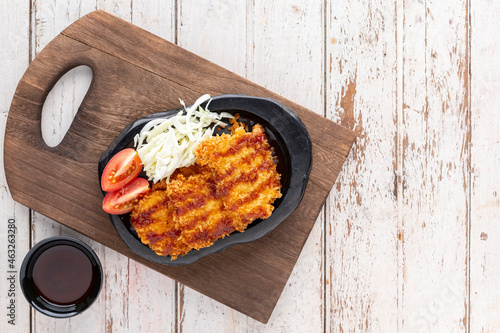 Japanese deep fried pork cutlet or Tonkatsu with sauce, cabbage and tomato in black ceramic plate on old wood cutting board on white wooden texture background with copy space for text, top table view