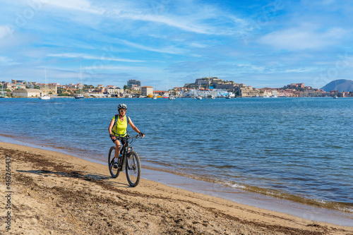 nice woman riding her electric mountain bike at the coastline of mediterranean sea on the Island of Elba in the tuscan Archipelago, in front of Porto Ferraio,Tuscany, Italy