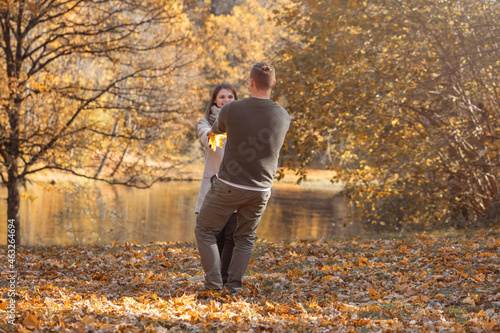 Love, leisure, nature, relationship concept. Young couple have fun on meadow with yellow leaves in the park with pond and trees during autumn sunset golden ours. Bright vivid backlight filter © Rytis